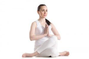 Sporty smiling beautiful young woman sitting in Gomukhasana, Cowface pose (yin yoga Shoelace posture) with hands in Namaste, studio full length shot on white background, three-quarters view, isolated